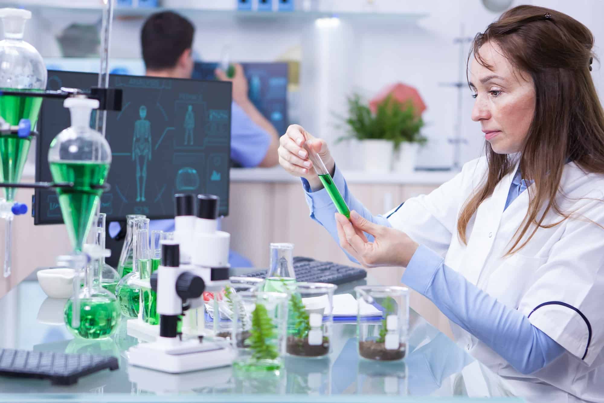Side view of female scientist doing research on plants holding a green solution in a test tube