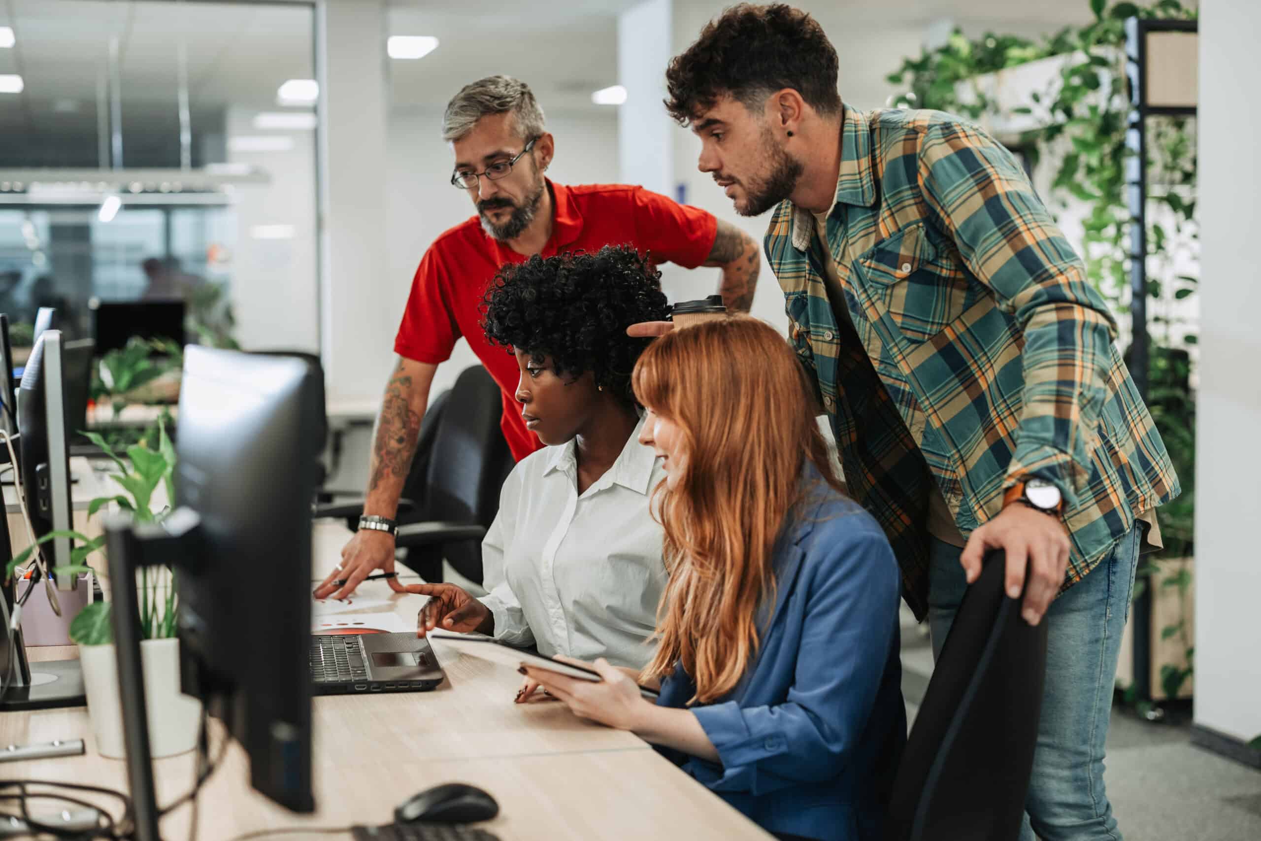 Business team of diverse professionals working together on laptops in a modern office, symbolizing collaboration, innovation, and effective tech recruitment strategies.