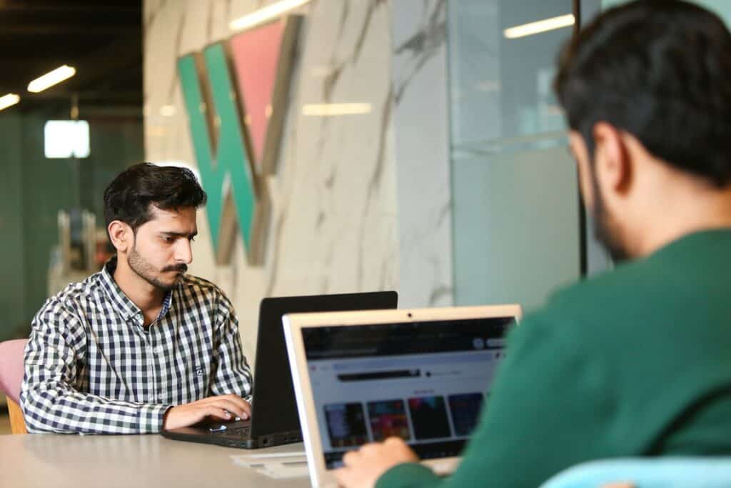 Two professionals collaborating on laptops in a contemporary office setting.